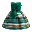 A sleeveless children's ball gown with a solid emerald green bodice and a flared skirt featuring horizontal stripes of green glitter, teal, white, and metallic gold, finished with a large bow at the waist, Obroi