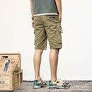 Person wearing khaki cargo shorts standing next to a wooden crate with a magazine on a white background, Obroi