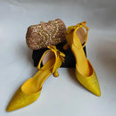 Yellow high-heeled shoes with decorative details and a matching clutch on a light gray background, Obroi
