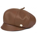 A brown faux-leather newsboy cap with a small gold logo badge on the side, displayed on a clean white background, Obroi