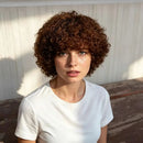 Woman with curly brown hair wearing a white t-shirt against a neutral background, Obroi