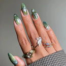 Hand with green nail polish and multiple rings on a neutral background, Obroi