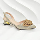 A single women's slingback pump in sparkling champagne gold glitter with a large layered gold fabric flower on the toe and a metallic gold heel accent, shown on a white wavy studio background, Obroi