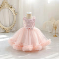 A toddler girl's formal party dress displayed on a mannequin in a bright, elegant room. The dress features a light pink sequined bodice with a large bow at the waist and a voluminous, layered tulle skirt in pale pink, Obroi