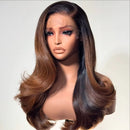 A long, wavy wig displayed on a mannequin bust against a plain light background. The wig has a dark brown root with warm caramel and honey brown highlights throughout, styled in loose, voluminous curls, Obroi