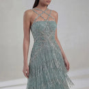 A model wearing a light blue-green beaded evening gown with silver fringe and crisscross halter-style straps, shown against a neutral studio background with the brand name Obroi in the top left corner, Obroi