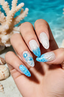 Nails with blue and white ocean-themed design against a coral background, Obroi