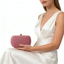 Woman in a white dress holding a pink glittery clutch against a white background, Obroi