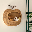 Woven apple-shaped pet bed with plush toys on a white wall, Obroi