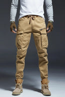 Person wearing tan cargo pants and brown boots on a gray background, Obroi