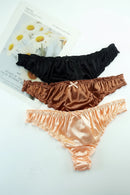 Three pairs of satin lingerie in black, brown, and peach on a white surface with a magazine in the background, Obroi