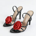 Black high-heeled shoes with red floral embellishments on a white background, Obroi