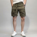 Person wearing olive green cargo shorts on a gray background, Obroi