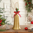 A gold Christmas bell decoration with a hanging loop, decorated with a red ribbon bow, pinecones, and greenery. The image includes dimension lines showing 21cm height, 11cm bell diameter, and a weight of 169g, set on a wooden table with holiday decorations in a festive room background, Obroi