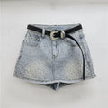 Light-wash denim mini skirt with a black belt and a silver rhinestone-embellished buckle, hanging on a clear plastic hanger against a white wall, Obroi