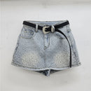 Light-wash denim mini skirt with a black belt and a silver rhinestone-embellished buckle, hanging on a clear plastic hanger against a white wall, Obroi