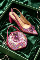 A pair of women's slingback peep-toe heels and a matching handbag, both in iridescent pink with purple crystal embellishments, displayed on a green velvet surface inside a green box with jewelry props, Obroi