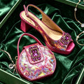 A pair of women's slingback peep-toe heels and a matching handbag, both in iridescent pink with purple crystal embellishments, displayed on a green velvet surface inside a green box with jewelry props, Obroi