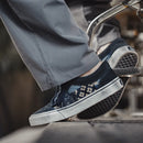 Person wearing navy slip-on shoes with floral patterns on a blurred background, Obroi