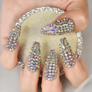 Nails with rhinestone decorations held by a hand against a neutral background, Obroi