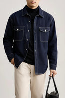 Person wearing a dark blue denim jacket over a black shirt on a light background, Obroi