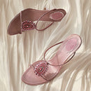 Pair of pink sandals with embellishments on a soft white fabric background, Obroi