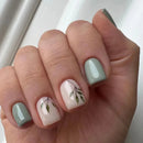 Hand with light green and white nails featuring leaf designs on a neutral background,Obroi