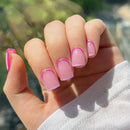 Hand with pink and white nail polish against a blurred natural background, Obroi