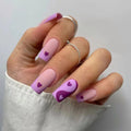 Hand with pink and purple nails featuring heart designs on a plain background, Obroi