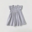 A light gray baby girl's dress with ruffled cap sleeves and vertical smocked pleats on the bodice, laid flat against a light gray background, Obroi