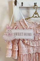 Decorative sign with a teddy bear and 'Sweet Home' text hanging on a white door with lace trim, Obroi