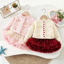 Two toddler girls' cardigan and tutu dress sets displayed on wooden hangers. The set on the left is light pink, featuring a pink knit cardigan with scalloped edges and pom-pom details, paired with a layered tulle tutu skirt, Obroi