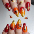 Close-up of manicured fingernails with a fall-themed design. The nails feature almond-shaped tips with glossy red and orange-to-yellow gradient tips, decorated with metallic gold foil leaf designs and a few black leaf accents, Obroi