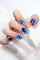 Hand with blue nail polish and floral designs on a white background, Obroi