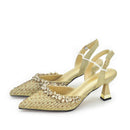 A pair of pointed-toe slingback heels in a glittering champagne gold fabric, embellished with rows of clear rhinestones across the toes and around the ankle straps, set against a plain white background, Obroi