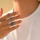 Person wearing a silver necklace with an eye-shaped pendant, Obroi
