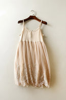 Beige dress with lace details on a wooden hanger against a white wall, Obroi