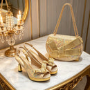 A pair of gold slingback high-heeled sandals with rhinestone bow details and a matching iridescent gold handbag with a chain strap, displayed on an ornate marble and gold console table beside a lit chandelier, Obroi
