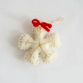 White felt snowflake ornament with a red bow on a light gray background, Obroi