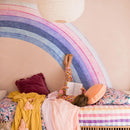 Person lying on a bed with a colorful rainbow headboard and pillows, Obroi