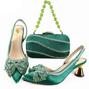 A coordinated women's formal accessories set in emerald green satin and embellished with rhinestones and crystal bows, including two pointed slingback high heels, a matching rhinestone clutch with a beaded shoulder strap, and a small green crystal bag, shown on a white background with the Obroi Party logo in the top left, Obroi