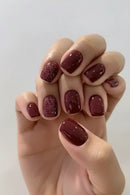 Hand with maroon and glittery nail polish on a plain background, Obroi