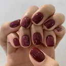 Hand with maroon and glittery nail polish on a plain background, Obroi