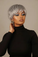 A woman taking a mirror selfie wearing a short, layered silver-gray wig, a black turtleneck, and gold geometric earrings against a solid beige background, Obroi