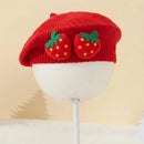 Red knit beret with strawberry decorations on a mannequin head against a beige background, Obroi