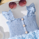 Light blue dress with ruffled details and pearl buttons, paired with red sunglasses on a white surface, Obroi
