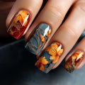 Nails with autumn-themed design featuring orange leaves and red accents on a dark background, Obroi