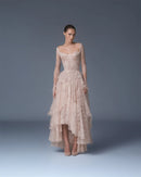 A model wearing a pale blush-beige lace high-low gown with long sheer sleeves and a structured bodice, standing against a smooth gray studio backdrop, Obroi
