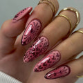 Obroi Hand with pink nail art and gold rings on a neutral background
