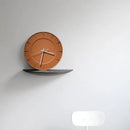 A minimalist wall clock with a terracotta-colored circular face and slim silver hands, mounted on a dark curved shelf against a light gray wall, Obroi